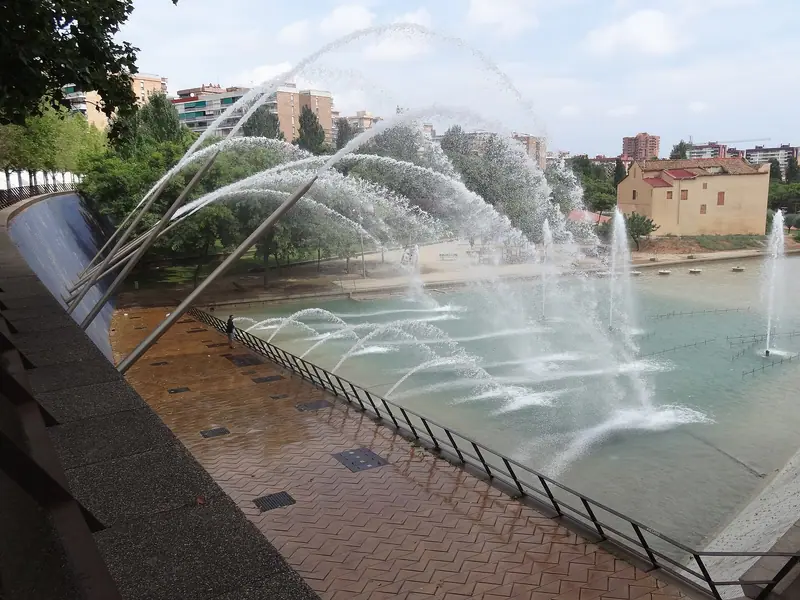 Chorros de agua sobre el estanque del Parc Central de Nou Barris, con la masia de Can Carreras al fondo
