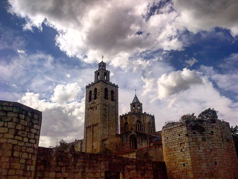 Torre campanario y muros de piedra del monasterio de Sant Cugat bajo un cielo nublado